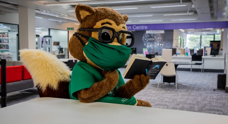 University Squirrel wearing a mask reading a book in the library